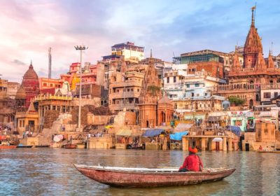 Ancient Varanasi city architecture and Ganges river ghat at sunset with view of an Indian sadhu sitting a boat on the river Ganges.